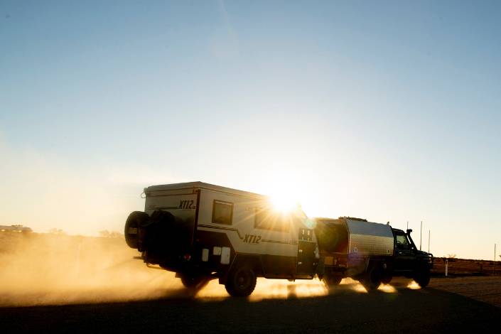 house sitter's 4WD towing a caravan across a dusty road with blue sky and the setting sun